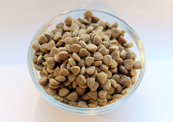 Dry balanced food for cats or dogs in a glass transparent bowl on a white background. Top view