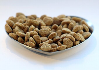 Dry cat food in a metal bowl in the shape of a heart on a white background