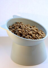 Dry cat food in a funny plastic bowl in the shape of a cat's head on a white background.