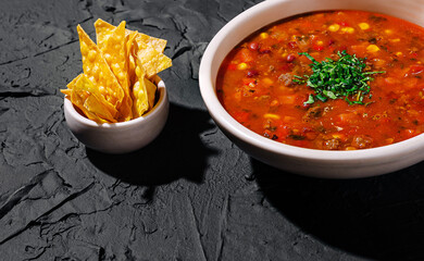 Chili served in a bowl with crispy tortilla chips on a dark background