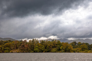 Lakeside scene with storm clouds over misty mountains and Autumn trees, Lake Windermere, The Lake...