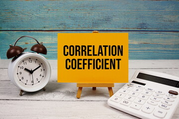 Correlation Coefficient text written on paper card with calculator and alarm clock on wooden background