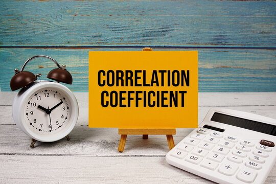 Correlation Coefficient text written on paper card with calculator and alarm clock on wooden background