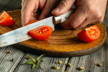 Fresh tomatoes are being sliced with a sharp knife on a rustic wooden cutting board in a bright...