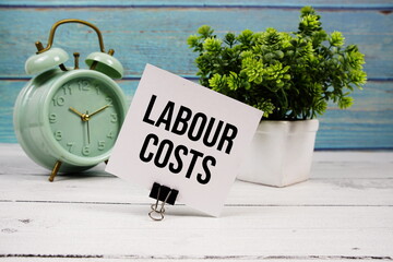 Labour Costs text written on paper card with alarm clock on wooden background