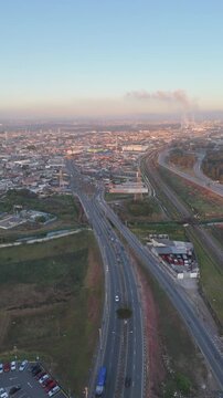 Vista a&eacute;rea de Mogi das Cruzes ao nascer do sol, com luz dourada iluminando pr&eacute;dios, montanhas ao fundo e a cidade ganhando vida.