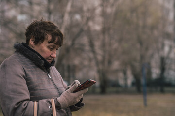 Elderly woman checking her phone in a park during late afternoon in a residential area