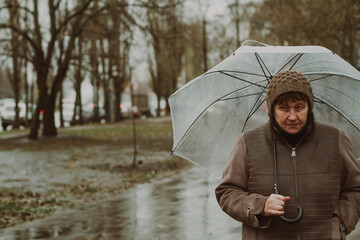 Thoughtful woman holding a transparent umbrella on a rainy day in an urban environment while...
