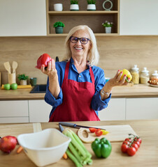 Portrait of happy senior mature woman prepering meal with fresh vegatebles in kitchen