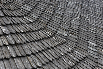 Close-up view of a textured wooden roof showcasing overlapping shingles arranged in a wavy pattern, highlighting the natural weathered appearance of the wood. neutral background, clear negative space