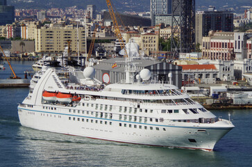 Luxury cruiseship cruise ship liner Breeze departure sail away from Barcelona, Spain during summer Mediterranean cruising with historic old town skyline in background and port infrastructure