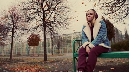 A woman sitting pensively on a bench in a park surrounded by trees during autumn - Powered by Adobe