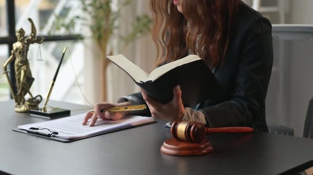 woman is sitting at a desk with a book and a pen. She is reading the book and she is focused on the content