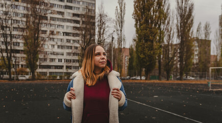 A young woman explores an urban park during an overcast day, surrounded by towering buildings and...