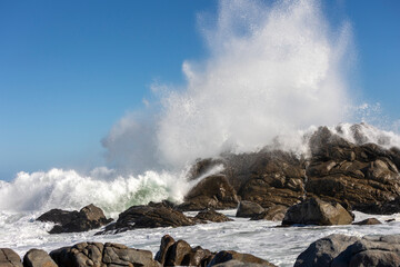 Big Ocean Wave Crashing Against Rock with Dramatic Splash Showing Power of the Sea under Clear Blue...
