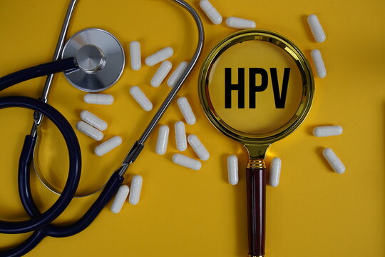 HPV abbreviation of Human Papilloma Virus text with Stethoscope and magnifying glass flat lay on yellow background