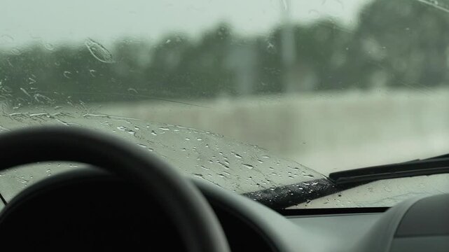 Rain Car Windshield: Rainy day view, wipers moving, water droplets obscure outside view.