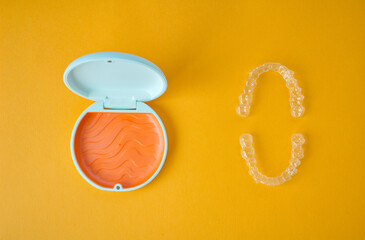 Clear Dental Aligners and Case on Orange Background. Orthodontic Mouthpieces.