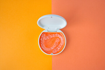 Clear Dental Aligners and Case on Orange and Pink Background. Orthodontic Mouthpieces.
