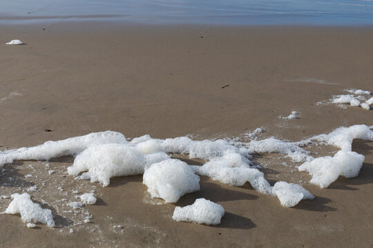 Mounds of sea foam on a sandy beach at the ocean's edge, environmental background, horizontal aspect