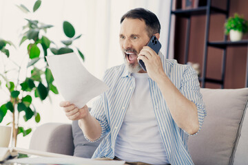 Excited senior man using smartphone while reviewing documents in a stylish home office with modern interior
