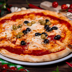 Delicious hot pizza with salmon, olives, tomatoes and spices on wooden table