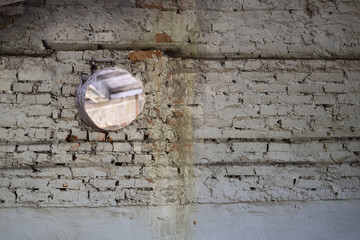 A round mirror mounted on a weathered brick wall, reflecting light and surroundings, showcasing the texture and imperfections of the surface. neutral background, clear negative space, clean, balanced
