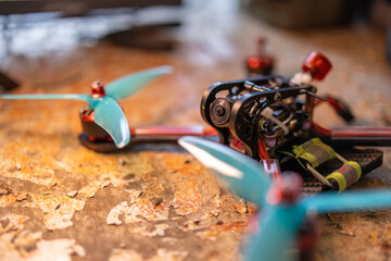 A close-up view of a FPV drone with turquoise propellers resting on a textured surface, showcasing its intricate components and design. neutral background, clear negative space, clean composition
