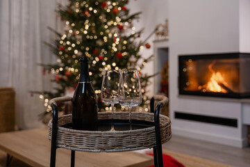 Champagne and glasses on a wicker tray in front of a decorated Christmas tree and fireplace