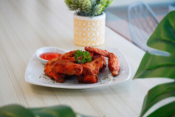 Spicy fried chicken served on a white plate with chili sauce and fresh herbs, presented on a wooden table with natural daylight. Authentic Indonesian comfort food concept featuring crispy chicken wing