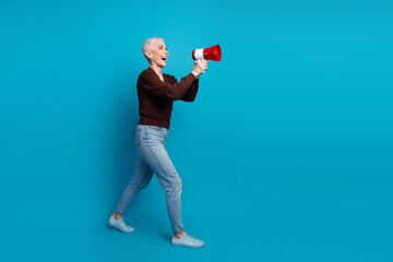 Happy mature woman with a megaphone promoting on blue background, demonstrating enthusiasm and charm in vibrant style