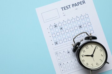 Student passing exam. Answer sheet and alarm clock on light blue background, flat lay. Space for text