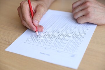 Student filling out multiple choice test at wooden table, closeup. Passing exam