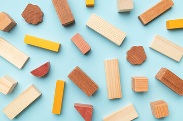 Wooden children's construction set blocks of different shapes natural colors on blue background. Montessori style cubes game for toddlers flat lay top view. Concept of learning and education
