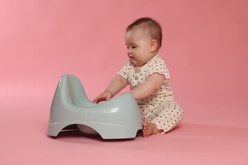 Cute little baby sitting near potty on pink background