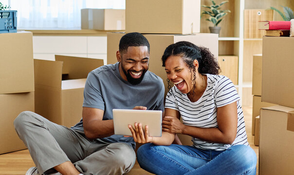 Portrait of a young couple unpacking, moving in and relocation to a new apartment, happy young couple using a tablet, browsing and shopping online, , family new beginning sitting on the floor