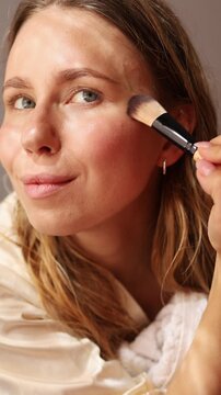 A model with natural beauty applies powder foundation to enhance her complexion. The setting is cozy and well-lit, showcasing effective techniques for a flawless finish.