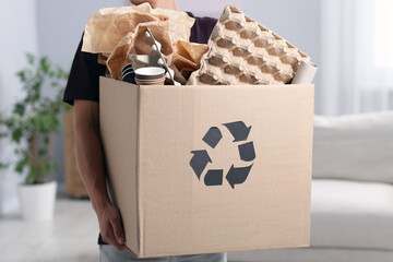 Recycling. Man holding cardboard box with different waste paper indoors, closeup