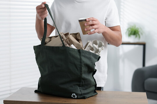 Recycling. Man putting waste paper into bag at wooden table indoors, closeup