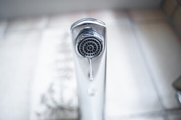 Dripping tap with water droplets inside apartment bathroom.