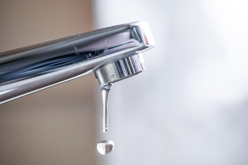 Dripping tap with water droplets inside apartment bathroom. Macro, close up shot, shallow depth of...