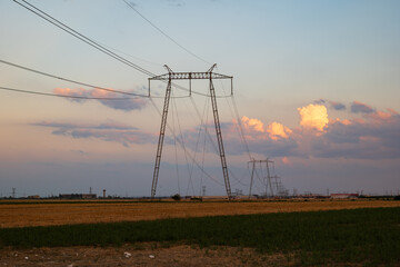 High voltage power line tower pole in a field at sunset.