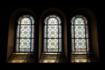 Backlit stained glass church windows with beautiful decorative colorful art. Interior wide angle view, moody light, no people