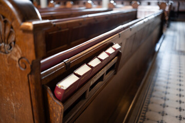 Small bible books in a shelf on the back of empty wooden pews inside church in Europe. Close up, wide angle shot, no people