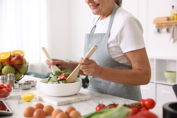 Senior woman cooking salad at white marble table in kitchen, closeup