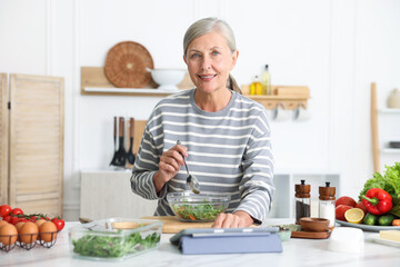 Senior woman using tablet while cooking at white marble table in kitchen
