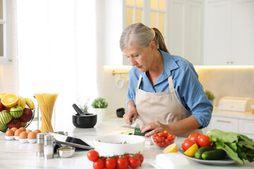 Senior woman cooking at white marble table in kitchen