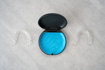 Clear dental aligner and blue case on marble table. Orthodontic mouthpiece storage.