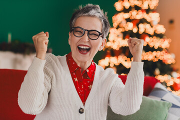 Joyful elderly woman celebrating Christmas at home with festive decorations and cheerful spirit...