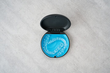 Clear dental aligner and blue case on marble table. Orthodontic mouthpiece storage.
